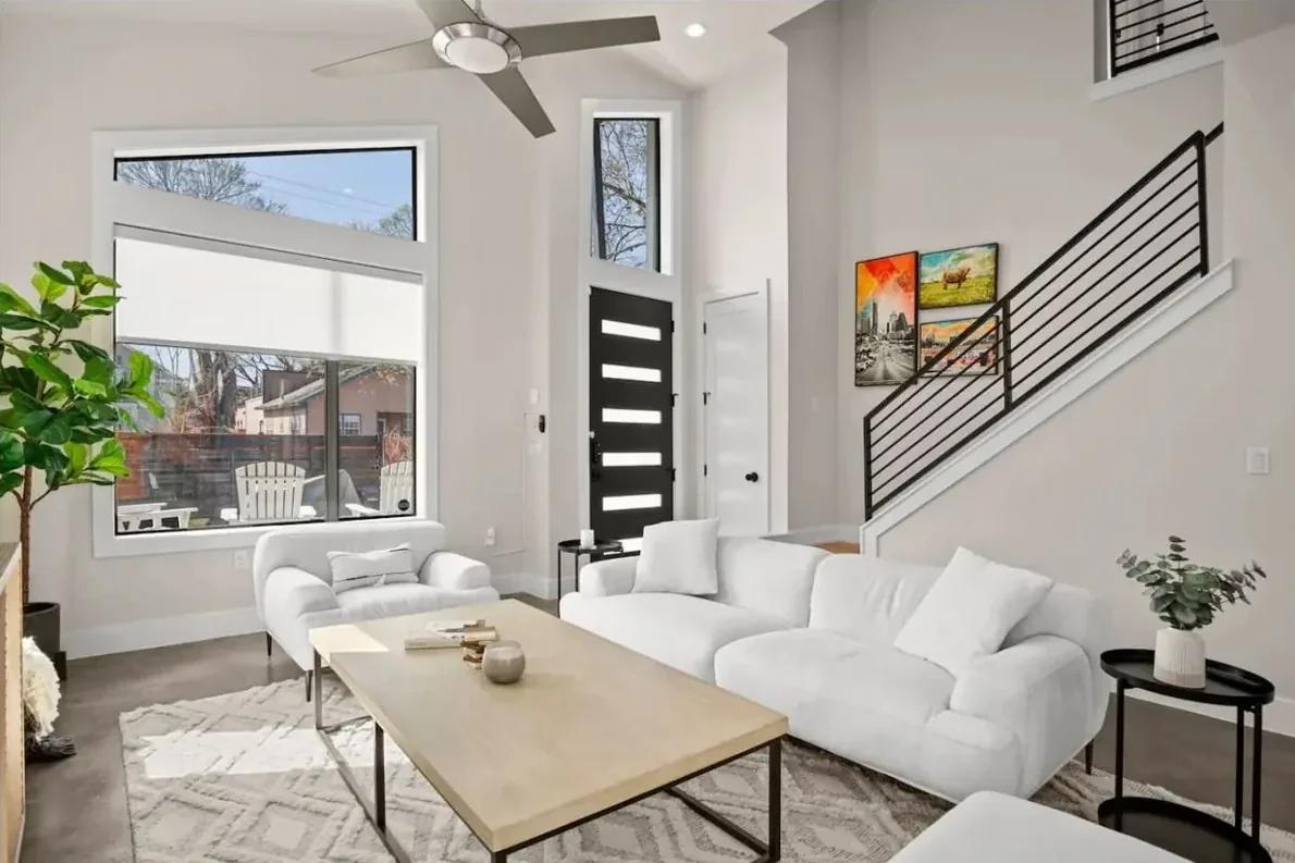 Bright Austin living room with white sofas, a coffee table, staircase, ceiling fan and tall windows